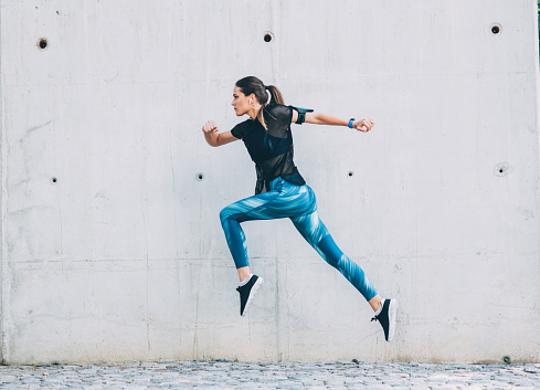 Sportswoman jumping in front of a wall outdoors.