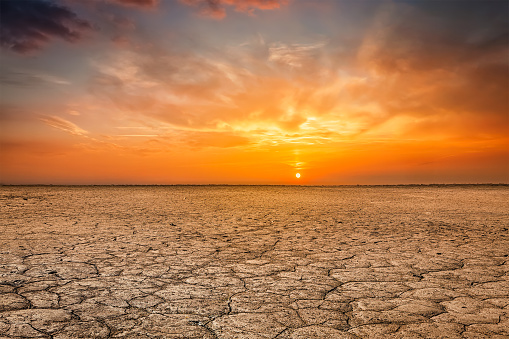 Global worming concept - cracked scorched earth soil drought desert landscape dramatic sunset