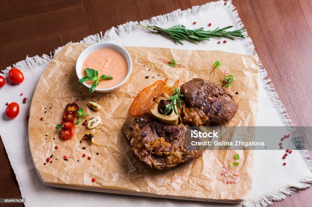 The large roasted piece of meat on the bone with sauce and spices on wooden board. View from top Bakery Stock Photo