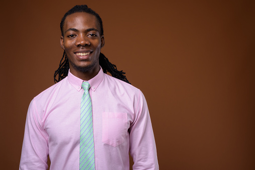 Studio shot of young handsome African businessman wearing pink shirt against colored background horizontal shot