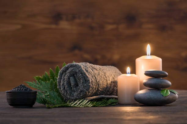 Spa treatment set Brown towel on green fern with candles and black hot stone on wooden background. Hot stone massage setting lit by candles. Hot stone therapy for one person with candle light. Beauty spa treatment and relax concept. spa massage stock pictures, royalty-free photos & images