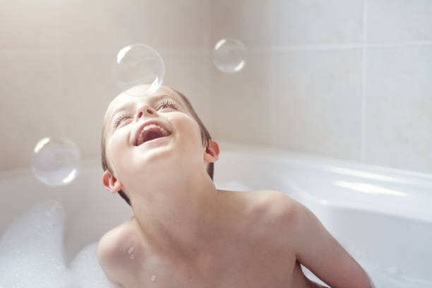 garçon jouant avec des bulles dans un bain de mousse - bubble child bubble wand blowing photos et images de collection