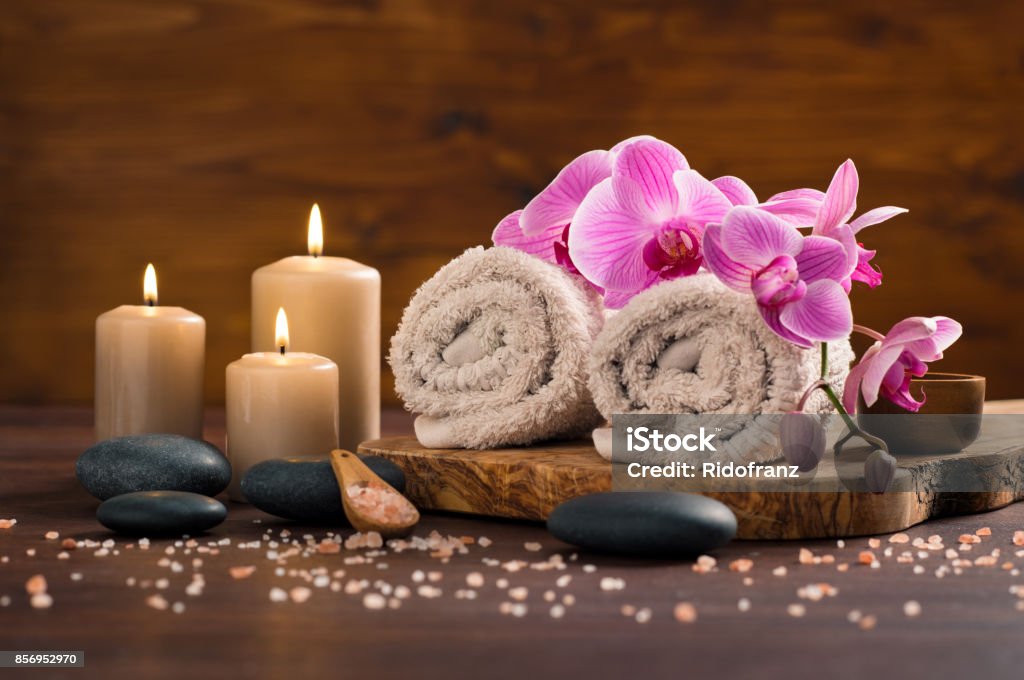 Spa and wellness setting Spa setting with brown rolled towel, orchids and candles on wood. Relaxing spa concept with candles, towels and hot stones massage with himalayan pink salt. Beautiful composition for beauty treatment in a spa. Spa Stock Photo