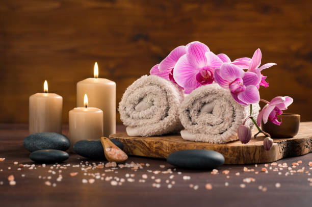 Spa and wellness setting Spa setting with brown rolled towel, orchids and candles on wood. Relaxing spa concept with candles, towels and hot stones massage with himalayan pink salt. Beautiful composition for beauty treatment in a spa. spas and spa treatments stock pictures, royalty-free photos & images