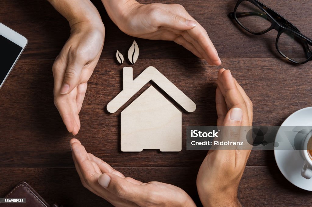 House care Top view of hands of a couple protecting their ecologigal house on wooden background. High angle view of hand of man and woman covering house shape. New home, Insurance and security concept. House Stock Photo