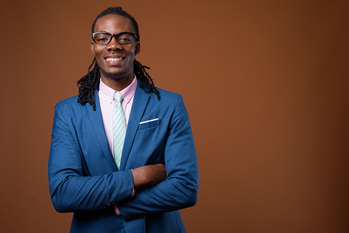 Studio shot of young handsome African businessman wearing blue suit and eyeglasses against colored background horizontal shot