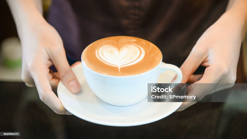 woman serving coffee while standing in coffee shop. Focus on Latte art hearth shape cup in female hands while placing of coffee on counter Heart Shape Stock Photo