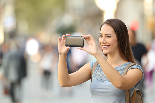 Single happy woman taking photos with a smart phone on the street