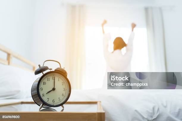 Closeup Alarm Clock Young Asian Woman Wake Up In The Moring And Stiing On Bed At Mirror Door Side Relaxing In Holiday With Sunlight Stock Photo - Download Image Now