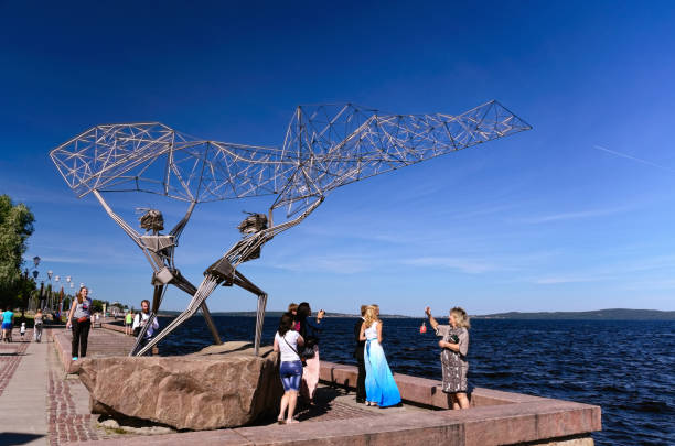 Petrozavodsk, Russia – August 22, 2015: Embankment at Lake Onega with Sculpture “Fishers Casting a Net” and Some People Walking About. The Sculpture Depicting a Russian Fisherman and an American One is a Gift from the City of Duluth in Minnesota, USA.