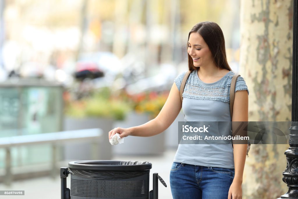 Civic woman throwing a paper into a trash bin Single civic woman throwing a paper into a trash bin on a city street Garbage Stock Photo