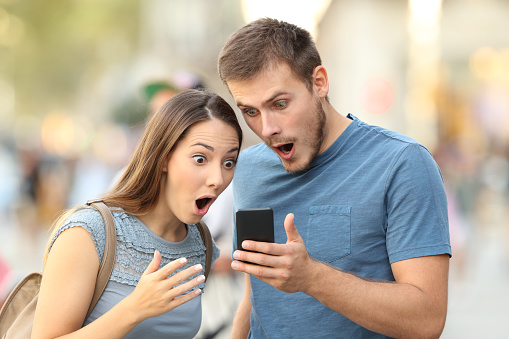 Amazed couple watching on line media in a smart phone standing on the street