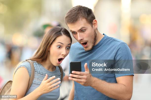 Amazed Couple Watching On Line Media In A Phone Stock Photo - Download Image Now - Surprise, Two People, Mobile Phone
