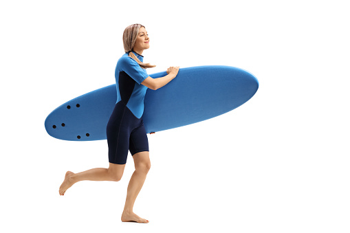 Full length profile shot of a woman in a wetsuit holding a surfboard and running isolated on white background