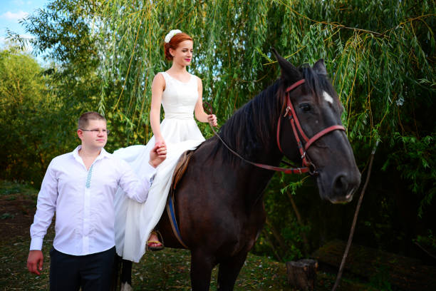 le marié mène le cheval par la bride. la mariée se trouve dans le saddl - adult beautiful wedding bride photos et images de collection