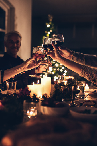 Close up shot of family toasting wine at christmas dinner. Family enjoying christmas dinner together at home, with focus on hands and wine glasses.