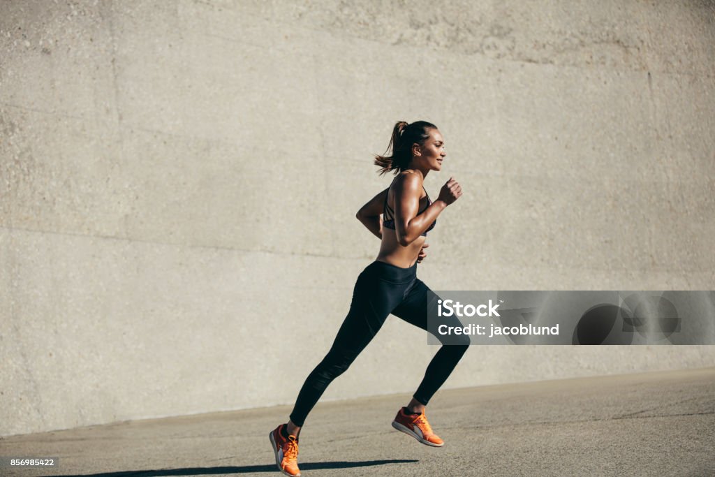 Healthy young woman on morning run Healthy young woman running in morning. Fitness model exercising in morning outdoors. Full length side view shot. Running Stock Photo
