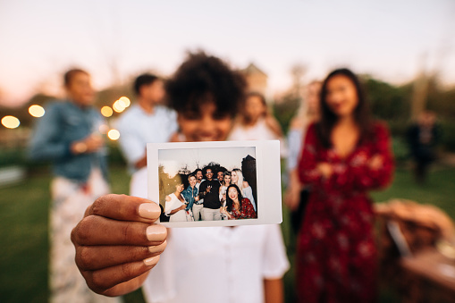 Woman showing picture in front with friends partying in background. Group photo of party people.