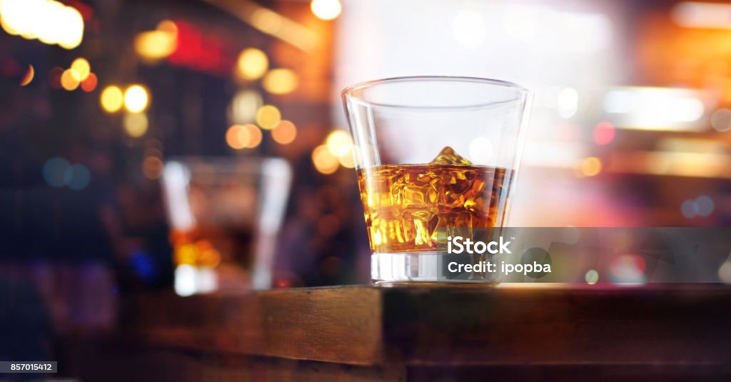 Glass of whiskey drink with ice cube on table wooden bar background Bar Counter Stock Photo