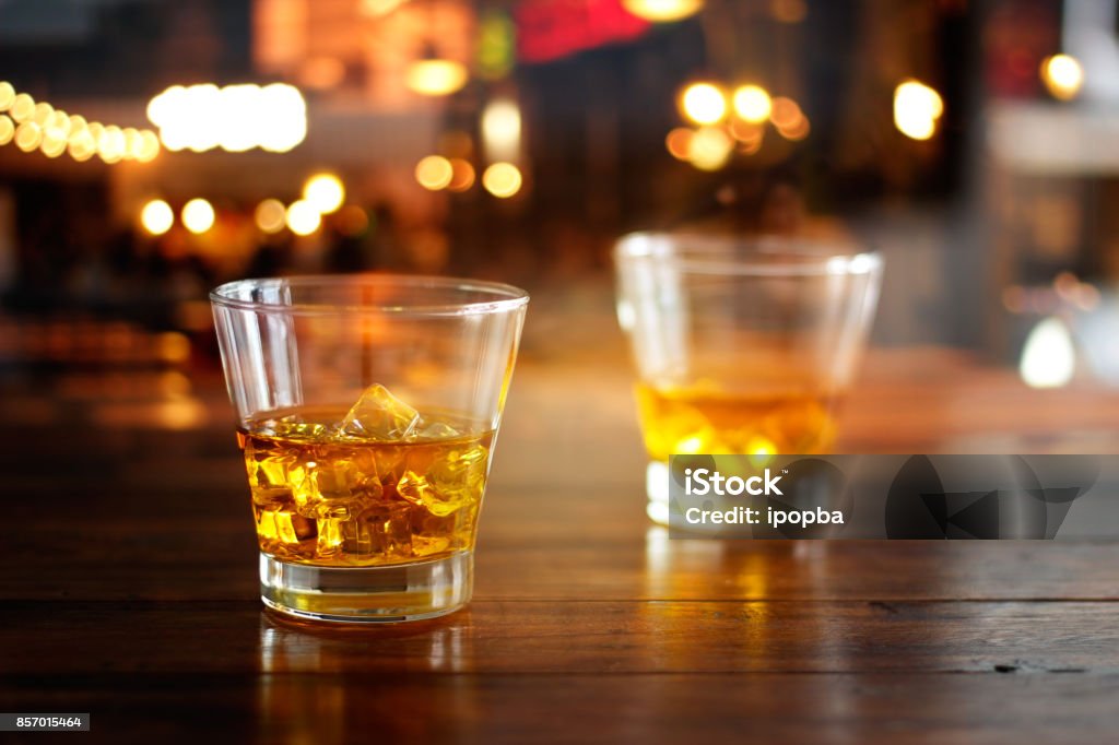 Whisky verre boisson avec le cube de glace sur une table en bois en bar de nuit coloré - Photo de Whisky libre de droits