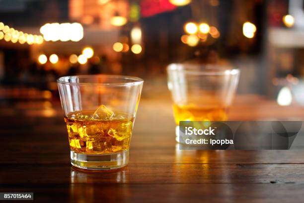 Whiskey Glass Drink With Ice Cube On Wooden Table In Colorful Night Bar Stock Photo - Download Image Now