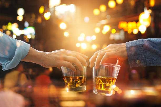 cheers звон друзей с бурбон виски пить в партии ночь после работы на красочном фоне - whisky alcohol glass party стоковые фото и изображения