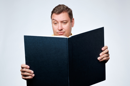 Caucasian man opening big book and with doubt looking in search of important information. Get education in mature age