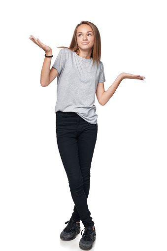 Doubtful teen girl standing in full length with two opened hand palms with blank copy spaces contemplating choosing weighing, isolated on white background