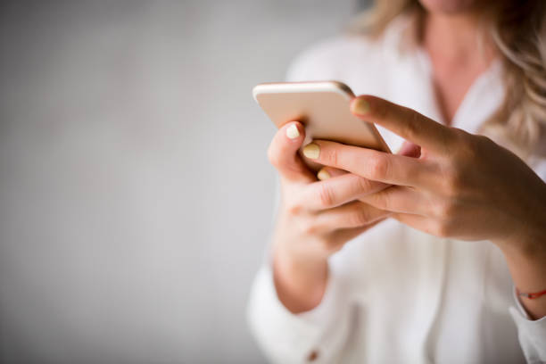 Using mobile phone Close up of a woman using her smartphone indoors. Holding stock pictures, royalty-free photos & images