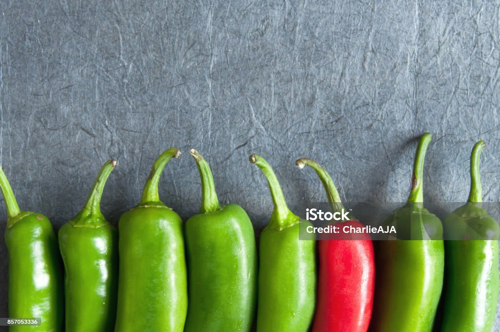 Chilli peppers Row of green chillis with one red pepper Standing Out From The Crowd Stock Photo