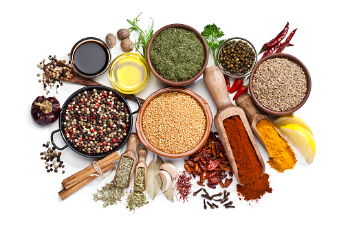 Top view of a large group of multi colored spices and herbs in bowls, wooden serving scoops or placed directly on the table shot on white background. Spices and herb included are clove, turmeric, bay leaf, cinnamon, olive oil, curry powder, nutmeg, peppercorns, chili pepper, basil, parsley, lemon, rosemary, garlic and saffron. DSRL studio photo taken with Canon EOS 5D Mk II and Canon EF 100mm f/2.8L Macro IS USM