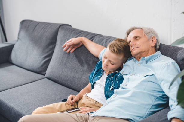 grandfather and grandson sleeping on sofa grandfather and grandson listening music with earphones and smartphone while sleeping on sofa sleeping grandpa stock pictures, royalty-free photos & images