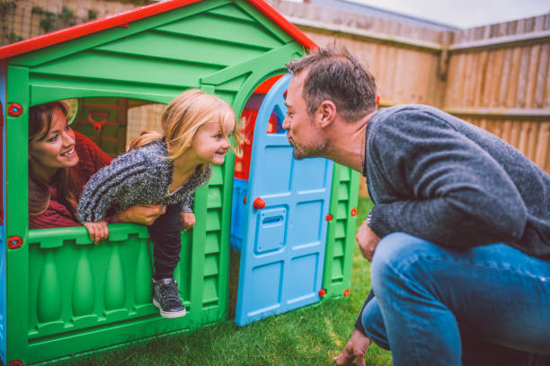 Kiss me daddy Little blond playful girl and her mother hiding in her playhouse in backyard. They are having fun. Her father is next to playhouse. kids play house stock pictures, royalty-free photos & images