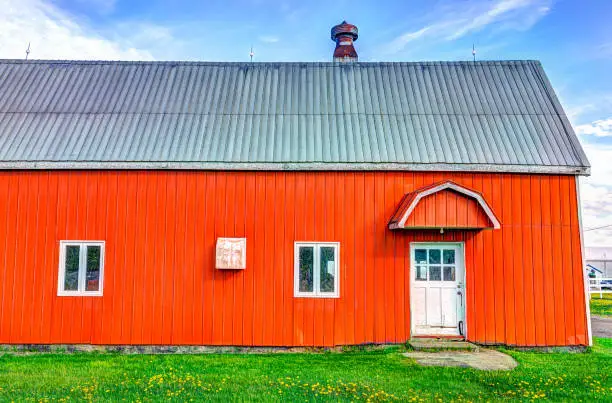 Red orange painted barn shed with white door in summer landscape field in countryside