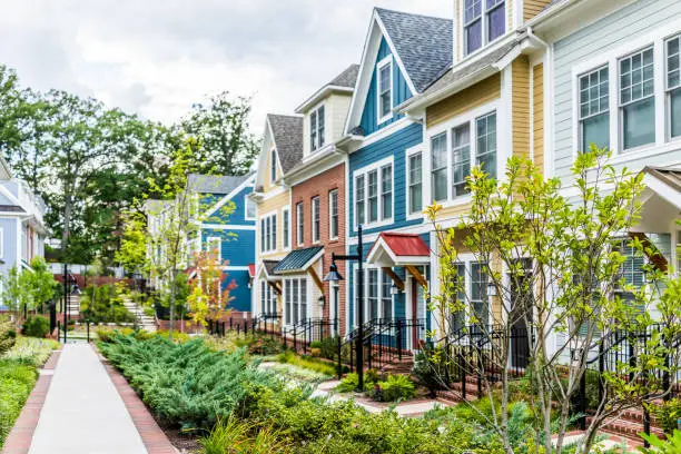 Photo of Row of colorful, red, yellow, blue, white, green painted residential townhouses, homes, houses with brick patio gardens in summer