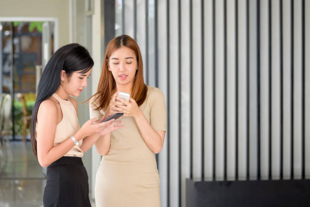istock two young beautiful Asian woman typing write message on smart phone 857087650