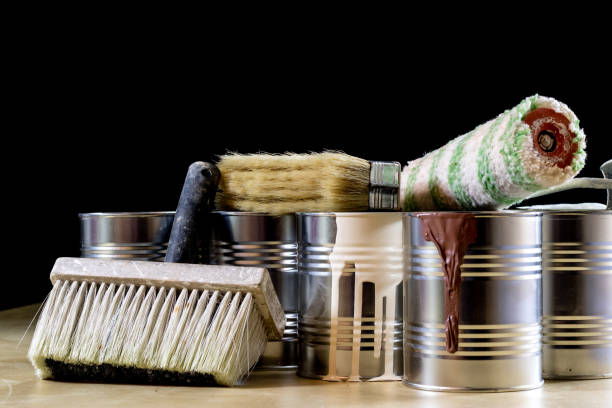 istock Cans of paint on a wooden workshop table. Next to the pedals and paint rollers. Black background 857097480