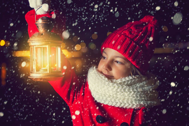 Beautiful little girl in a red winter coat walking through the snowy night with lantern