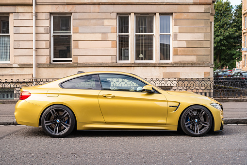 A metallic yellow coloured BMW M4 sports coupe parked on a street in Glasgow, Scotland, UK.