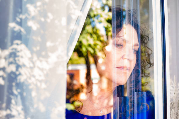 istock Mature Caucasian female looking cautiously out of a window 857103436