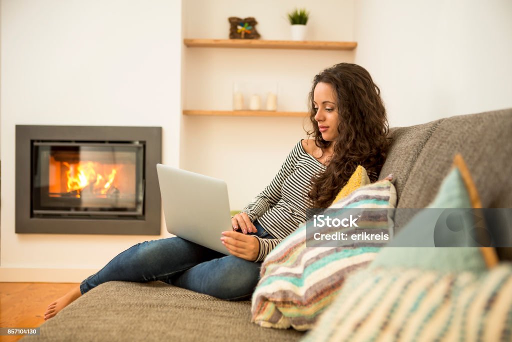 Working at home Beautiful woman working with a laptop at the warmth of the fireplace Fireplace Stock Photo