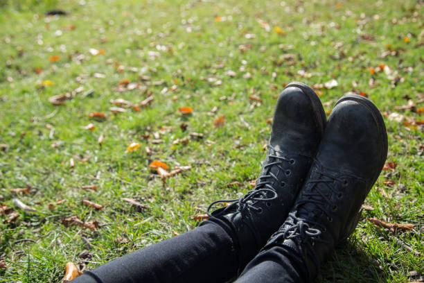 A photograph of a girls black boots and pants in the grass.