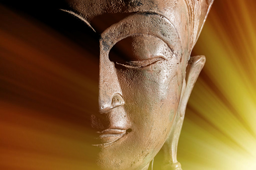 Zen Buddhism. Divine light rays of spiritual enlightenment or astral projection on buddha head statue.