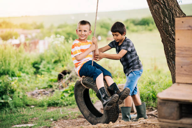 two boys playing with a tire swing - freedom tire swing tire swing imagens e fotografias de stock