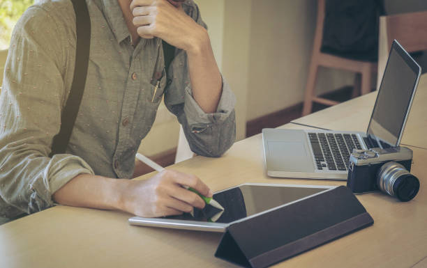 istock Close-up of male hand, using digital tablet, computer and camera while sitting at his working place. 857156756