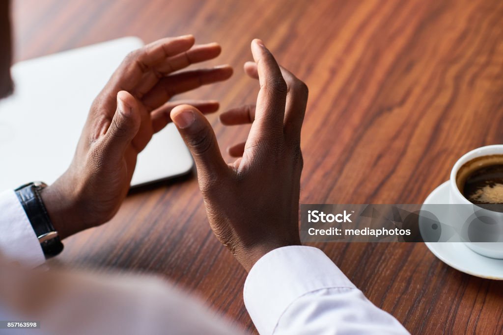 Man gesturing while explaining Close-up of unrecognizable African businessman gesturing while speaking his mind at informal meeting in restaurant Discussion Stock Photo