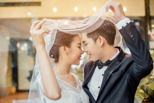 Asian groom and Asian bride are under viel together and are about to kiss each other with a smiling and happy face.