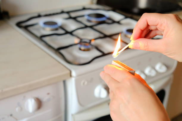 a woman with lighted match with gas litted stove behind - fire match women flame imagens e fotografias de stock