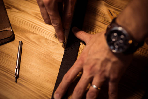istock Working process of the leather belt in the leather workshop. Man holding crafting tool and working. Tanner in old tannery. Wooden table background. Close up man arm 857218838