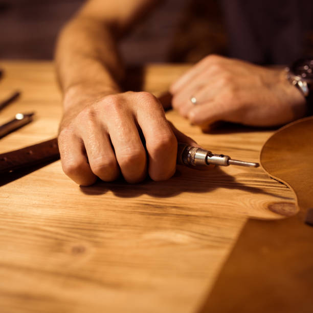 istock Working process of the leather belt in the leather workshop. Man holding crafting tool and working. Tanner in old tannery. Wooden table background. Close up man arm 857218920